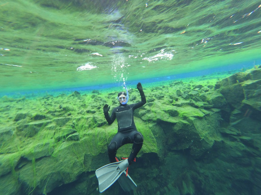 Persona haciendo snorkel en Silfra, Islandia. Detrás se ve la Laguna Azul.