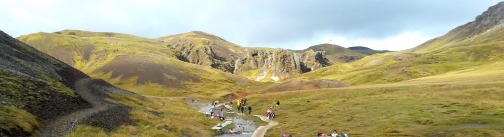 Se puede apreciar la parte media del río termal donde hay gente bañándose y las montañas del valle Reykjadalur que lo rodean.